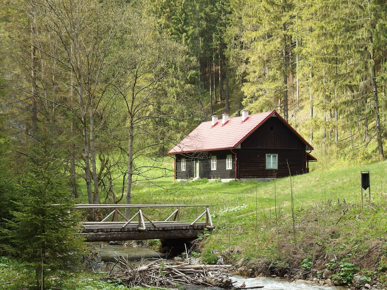 Drevená horáreň s červenou strechou pri potoku na okraji lesa